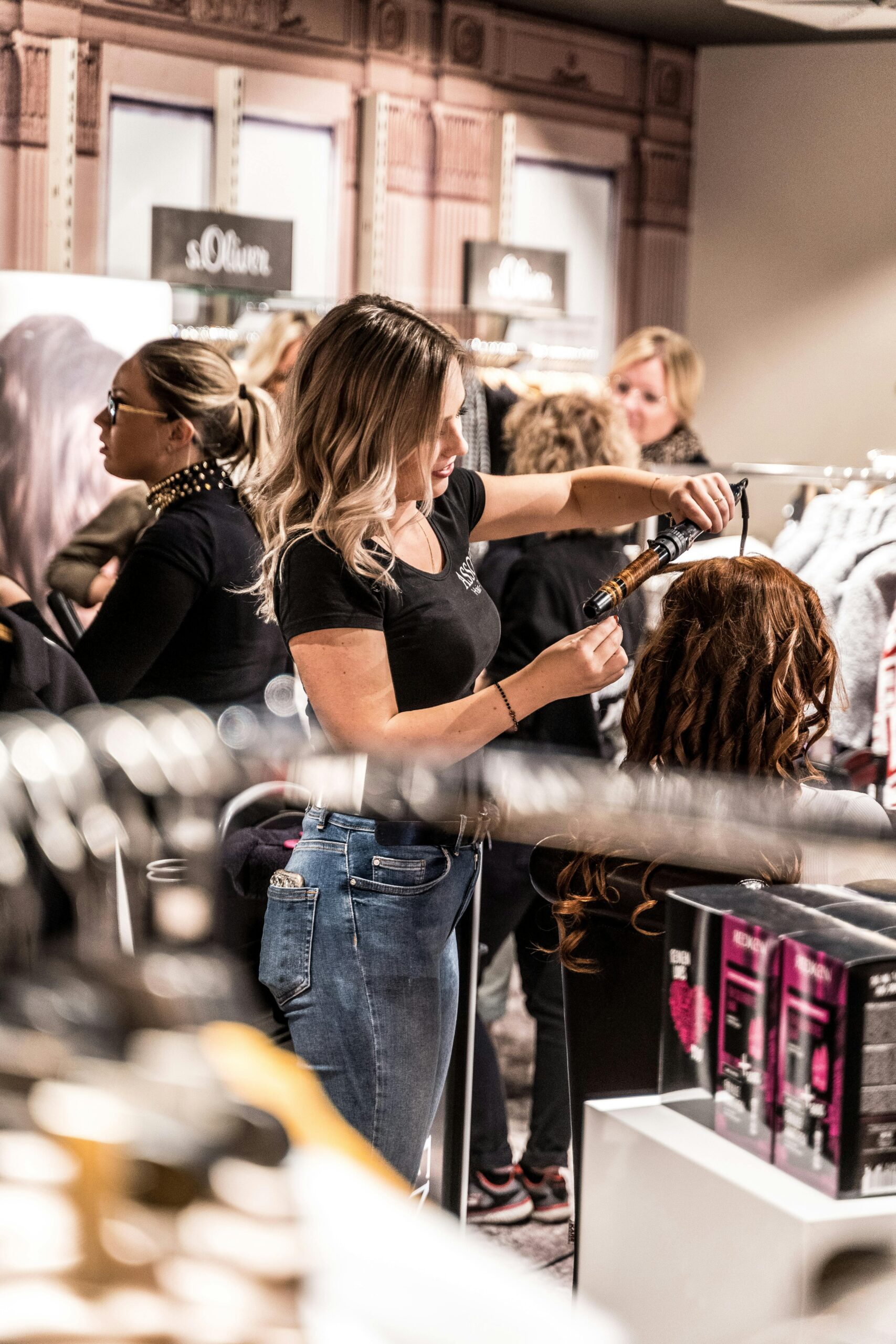 A skilled hairstylist uses a curling iron to style a client's hair in a busy salon.